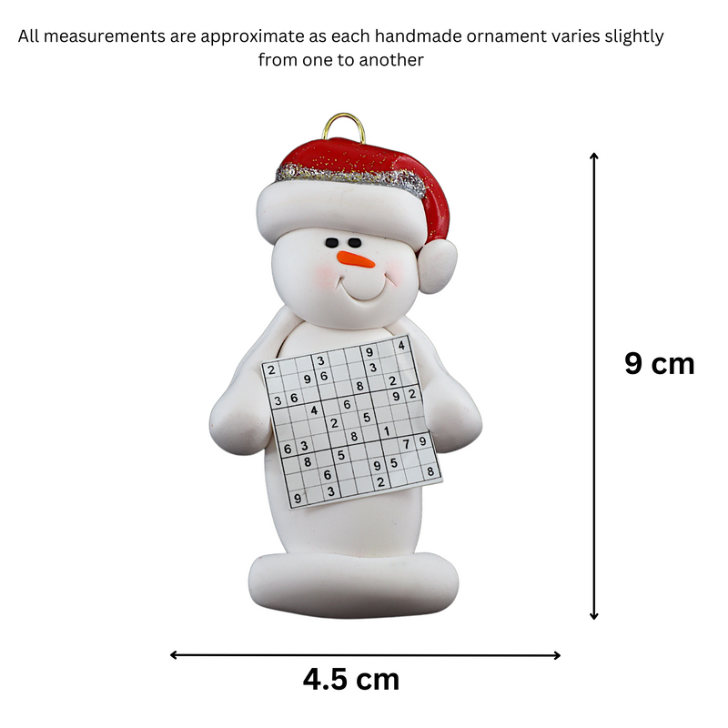 Ornament of white snowman in red hat holding a sudoku page, graphed to show size (4.5x9cm).