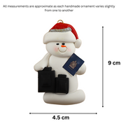 Ornament of white snowman in red hat holding a passport and suitcases, graphed to show size (4.5x9cm).