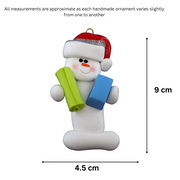 Ornament of white snowman in red hat holding vibrant yoga mat and block, graphed to show size (4.5x9cm).