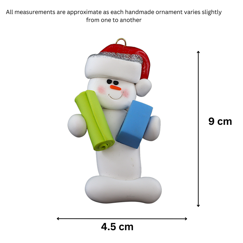 Ornament of white snowman in red hat holding vibrant yoga mat and block, graphed to show size (4.5x9cm).