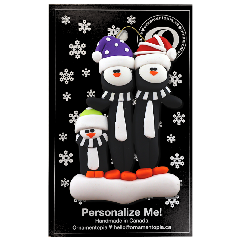 Family ornament with 3 black and white penguins in colourful festive hats, on display backing card.