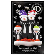 Family ornament with 4 black and white penguins in colourful festive hats, on display backing card.