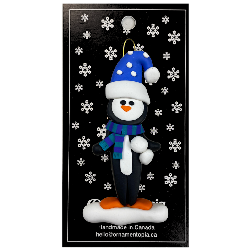 Penguin wearing blue hat and scarf ornament, on display backing card.