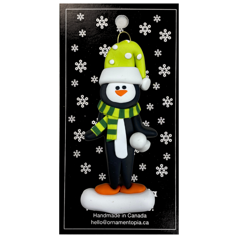 Penguin wearing green hat and scarf ornament, on display backing card.