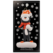 Penguin wearing orange hat and scarf ornament, on display backing card.