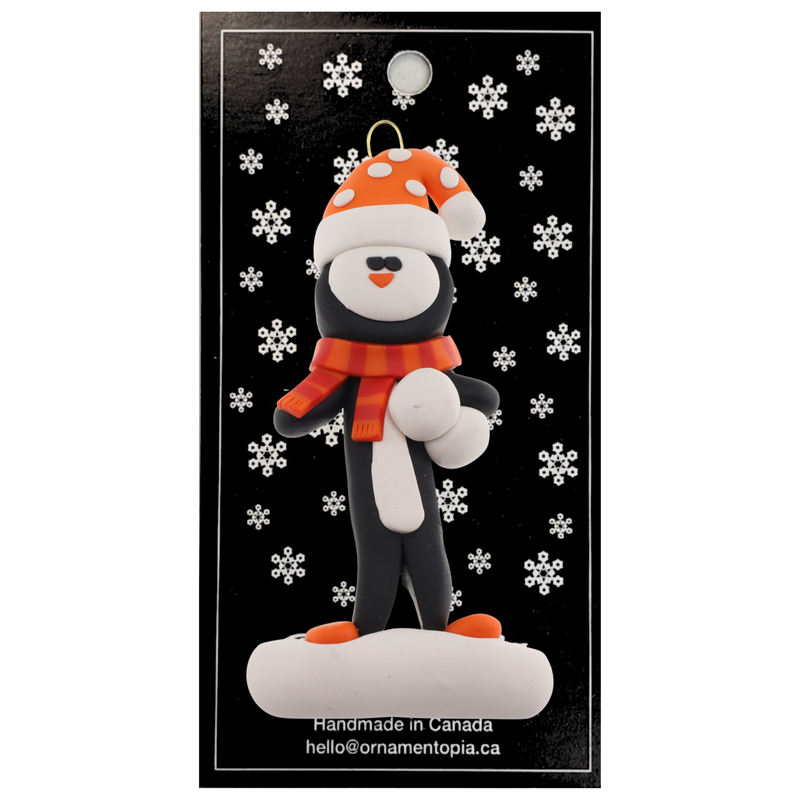 Penguin wearing orange hat and scarf ornament, on display backing card.