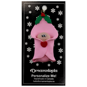 Ornament with an infant head poking out of a pink baby blanket, on display backing card.