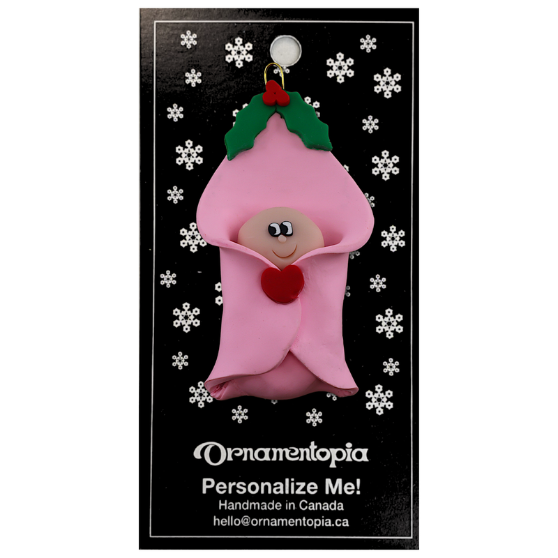 Ornament with an infant head poking out of a pink baby blanket, on display backing card.
