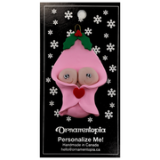 Ornament with twin infant heads poking out of a pink baby blanket, on display backing card.