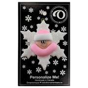 Baby ornament with infant face and pink hat on glittery white snowflake base, on display backing card.