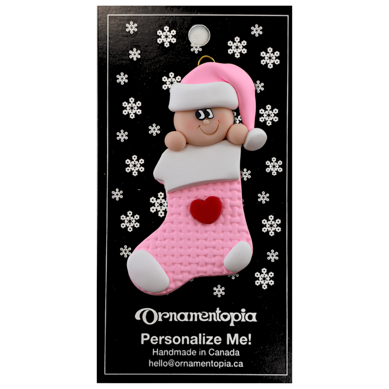 Ornament with infant head in a pink hat poking out of a pink stocking, on display backing card.