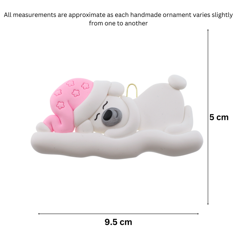 Ornament of white sleeping polar bear baby in a pink hat, graphed to show size (9.5x5cm).