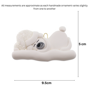 Ornament of white sleeping polar bear baby in a white sparkling hat, graphed to show size (9.5x5cm).