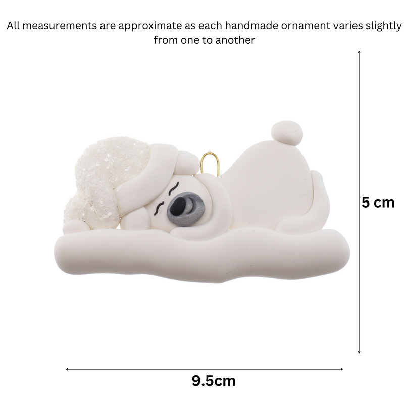 Ornament of white sleeping polar bear baby in a white sparkling hat, graphed to show size (9.5x5cm).