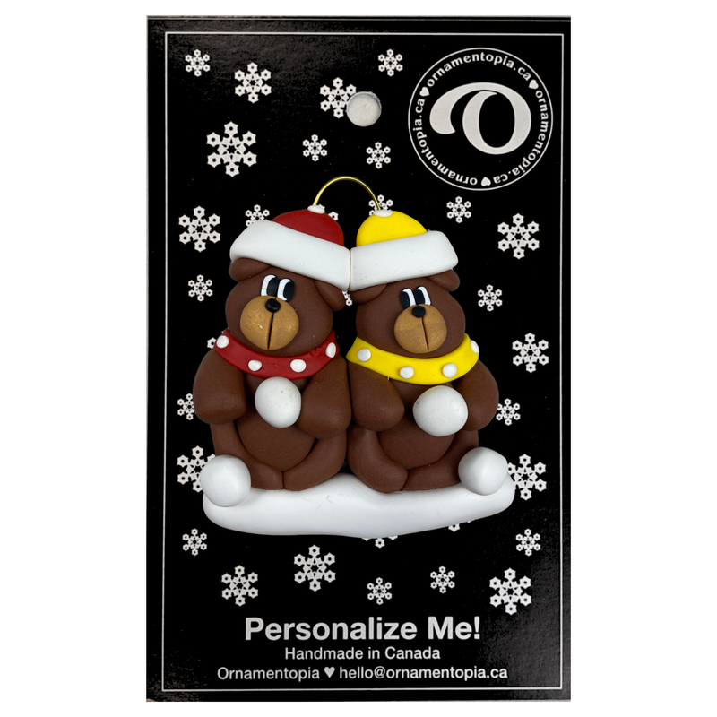 A couple’s ornament of two brown bears in polka dot scarves and hats, on display backing card.