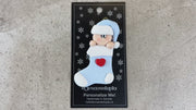 Ornament with infant head in a blue hat poking out of a blue stocking, shown on backing card and Christmas tree.