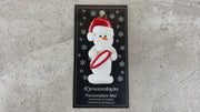 Ornament of white snowman in red hat holding a red and white rugby ball, shown on backing card and Christmas tree.