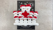 Family ornament with 11 white snowmen in red hats, gathered around a red maple leaf, shown on backing card and Christmas tree.