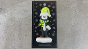 Penguin wearing green hat and scarf ornament, shown on backing card and Christmas tree.