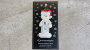 Ornament of white snowman in red hat holding an eye chart, shown on backing card and Christmas tree.