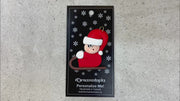 Small figure in red outfit and festive hat riding on brown toboggan ornament, shown on backing card and Christmas tree.
