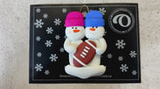 Family ornament with 2 white snowmen in bright hats with a football, shown on backing card and Christmas tree.