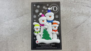 Family ornament with 4 white snowmen in bright scarves, with green Christmas tree, shown on backing card and Christmas tree.
