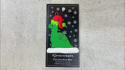 Green dinosaur wearing red festive hat ornament, shown on backing card and Christmas tree.