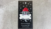 Ornament of grey dog in red hat hanging on a white bone, shown on backing card and Christmas tree.