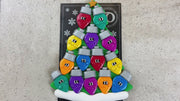 Christmas tree ornament decorated with 14 light bulbs with smiling faces, shown on backing card and decorated Christmas tree.