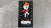 Penguin wearing orange hat and scarf ornament, shown on backing card and Christmas tree.