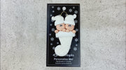Ornament with twin infant heads in white glitter hats poking out of a white glitter stocking, shown on backing card and Christmas tree.