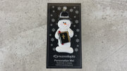 Ornament of white snowman in black top hat, holding a Bible, shown on backing card and Christmas tree.