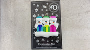 Family ornament with 3 white snowmen in colourful hats holding matching presents, shown on backing card and Christmas tree.