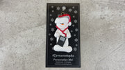 Ornament of white snowman in red hat holding an i-pod with headphones, shown on backing card and Christmas tree.