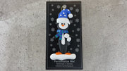 Penguin wearing blue hat and scarf ornament, shown on backing card and Christmas tree.