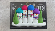 Family ornament with 4 snowmen in colourful scarves, hemmed by Christmas trees, shown on backing card and Christmas tree.