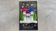 Ornament with 3 snowmen in colourful scarves and hats, hemmed by Christmas trees, shown on backing card and Christmas tree.