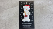 Ornament of white snowman in red hat holding a toilet plunger, shown on backing card and Christmas tree.