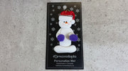 Ornament of white snowman in red hat holding purple cheerleader pom-poms, shown on backing card and Christmas tree.