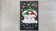A couple’s ornament of two small white snowmen beside a festive brown house, shown on backing card and Christmas tree.