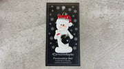 Ornament of white snowman in red hat holding a black bowling ball and pin, shown on backing card and Christmas tree.