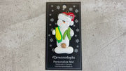 Ornament of white snowman in red hat holding various colourful vegetables, shown on backing card and Christmas tree.
