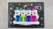 Family ornament with 4 white snowmen in colourful hats holding matching presents, shown on backing card and Christmas tree.