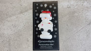 Ornament of white snowman in red hat holding a white ambulance, shown on backing card and Christmas tree.