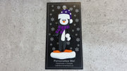 Penguin wearing purple hat and scarf ornament, shown on backing card and Christmas tree.