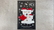 Family ornament with 3 white snowmen in red hats, gathered around a red maple leaf, shown on backing card and Christmas tree.