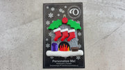 Vibrant fireplace ornament with holly and presents, displaying 3 red stockings, shown on backing card and Christmas tree.