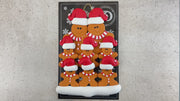 Family ornament with 8 brown gingerbread figures in red Christmas hats, shown on backing card and Christmas tree.