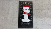 Ornament of white snowman in red hat holding red cheerleader pom-poms, shown on backing card and Christmas tree.